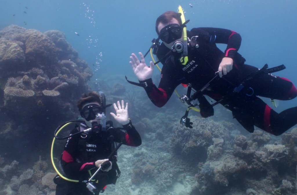 A Scuba Woman and a scuba man waving underwater