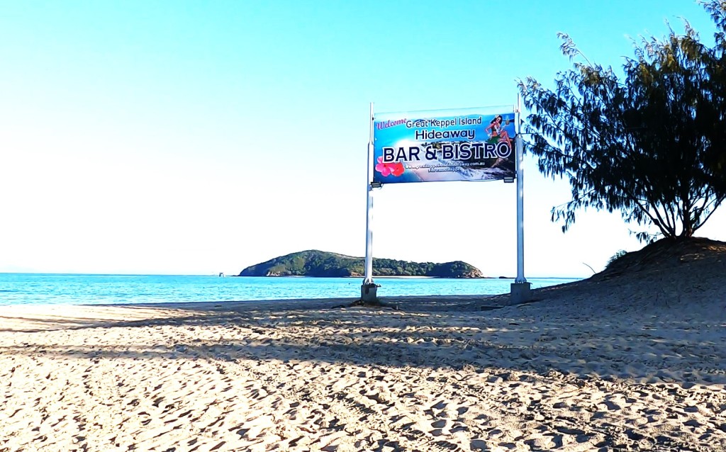 View from Great Keppel Island with an island in the background and a sign saying Hideaway Bar & Bistro.